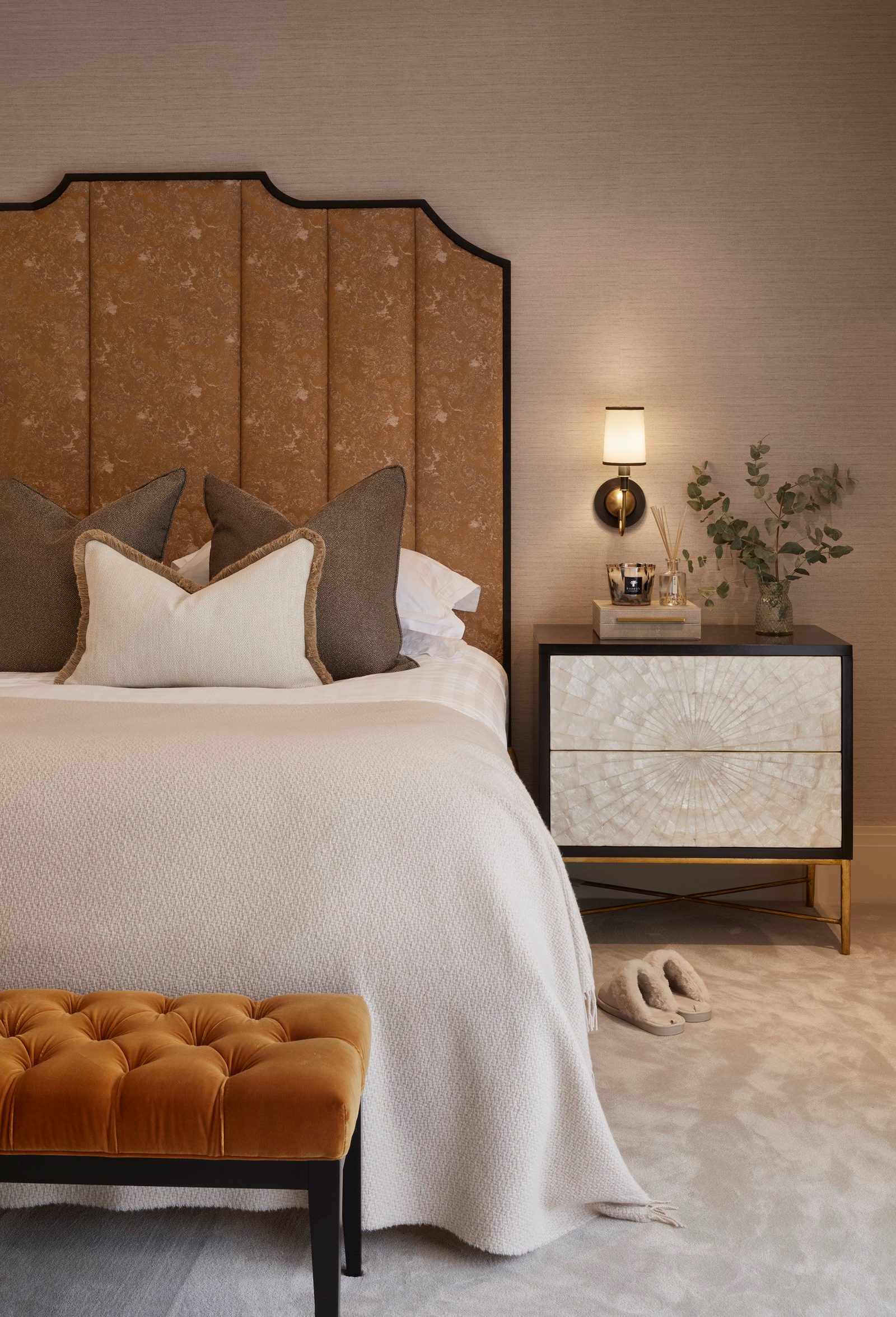 Bed with ochre headboard, fringed cushions and a brass wall light