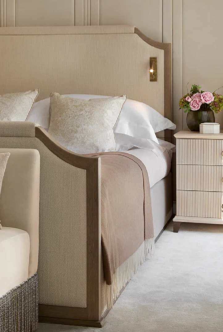 An upholstered bed with a curved headboard and fringed base