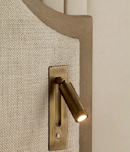 A brass reading light on a bouclé headboard