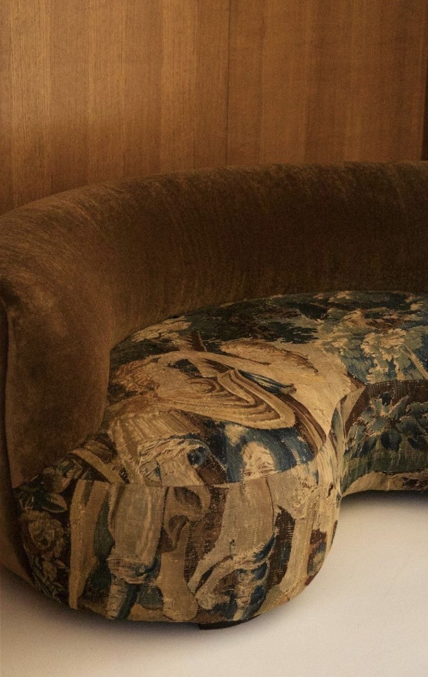 A curved sofa upholstered in antique tapestry