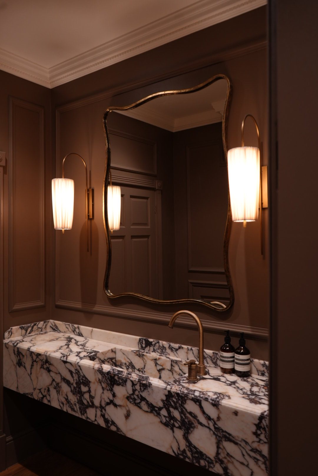 Wall-to-wall marble vanity with antique bronze tap, shaped mirror and wall lights at the Radlett Residence