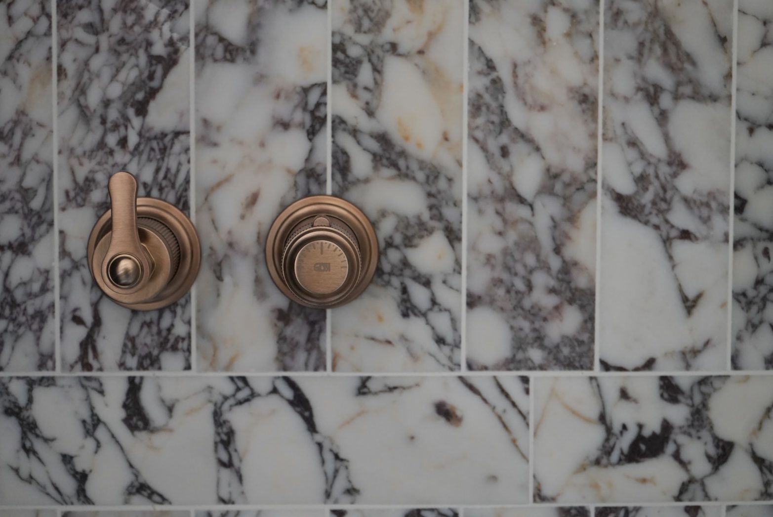 Bronze shower valves set in book-matched marble at the Tewin Family Home